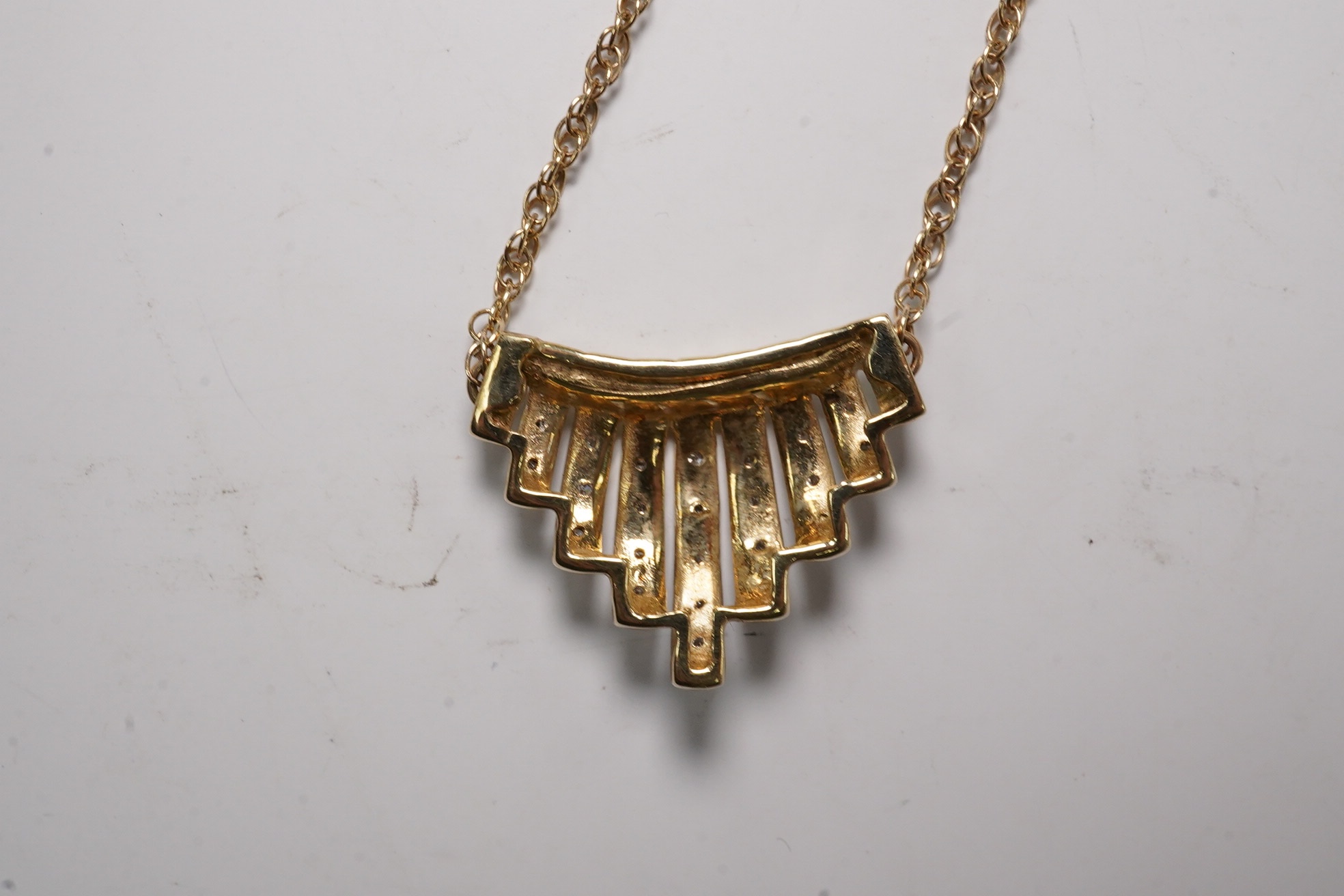 A yellow metal and diamond chip set fan shaped pendant, width 22mm, on a 375 chain, 40cm, gross 5.6 grams.